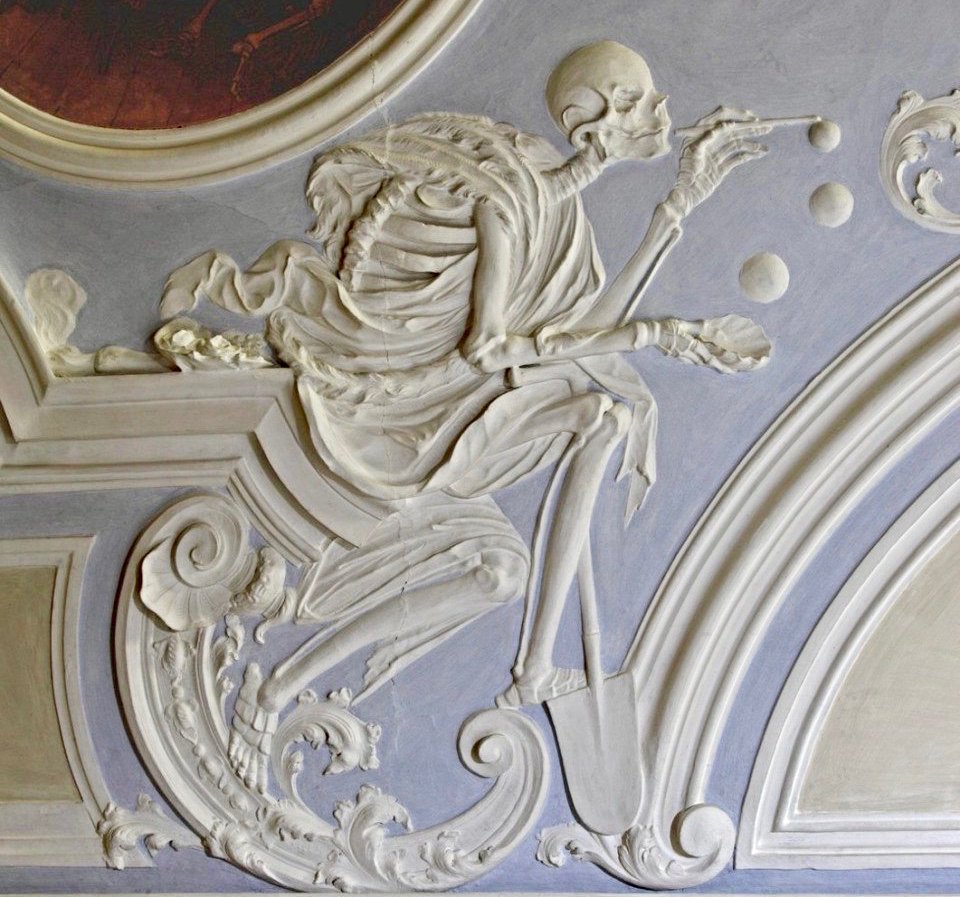 a plaster relief showing a skeleton in a toga blowing bubbles